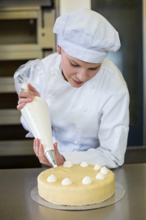 Baker prepares cake in bakehouse with whipped cream